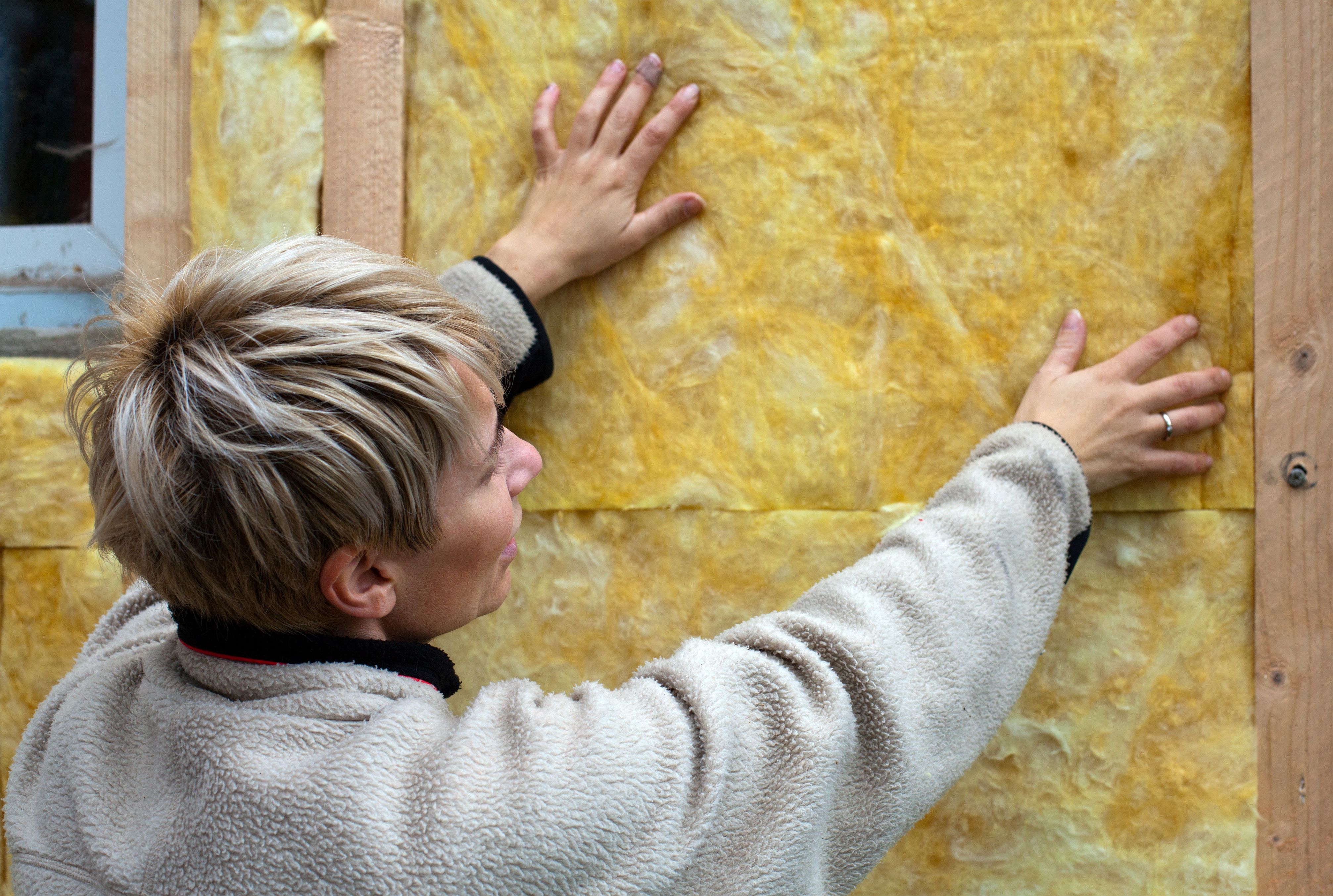  Frau bringt Dämmung an Fassade an 