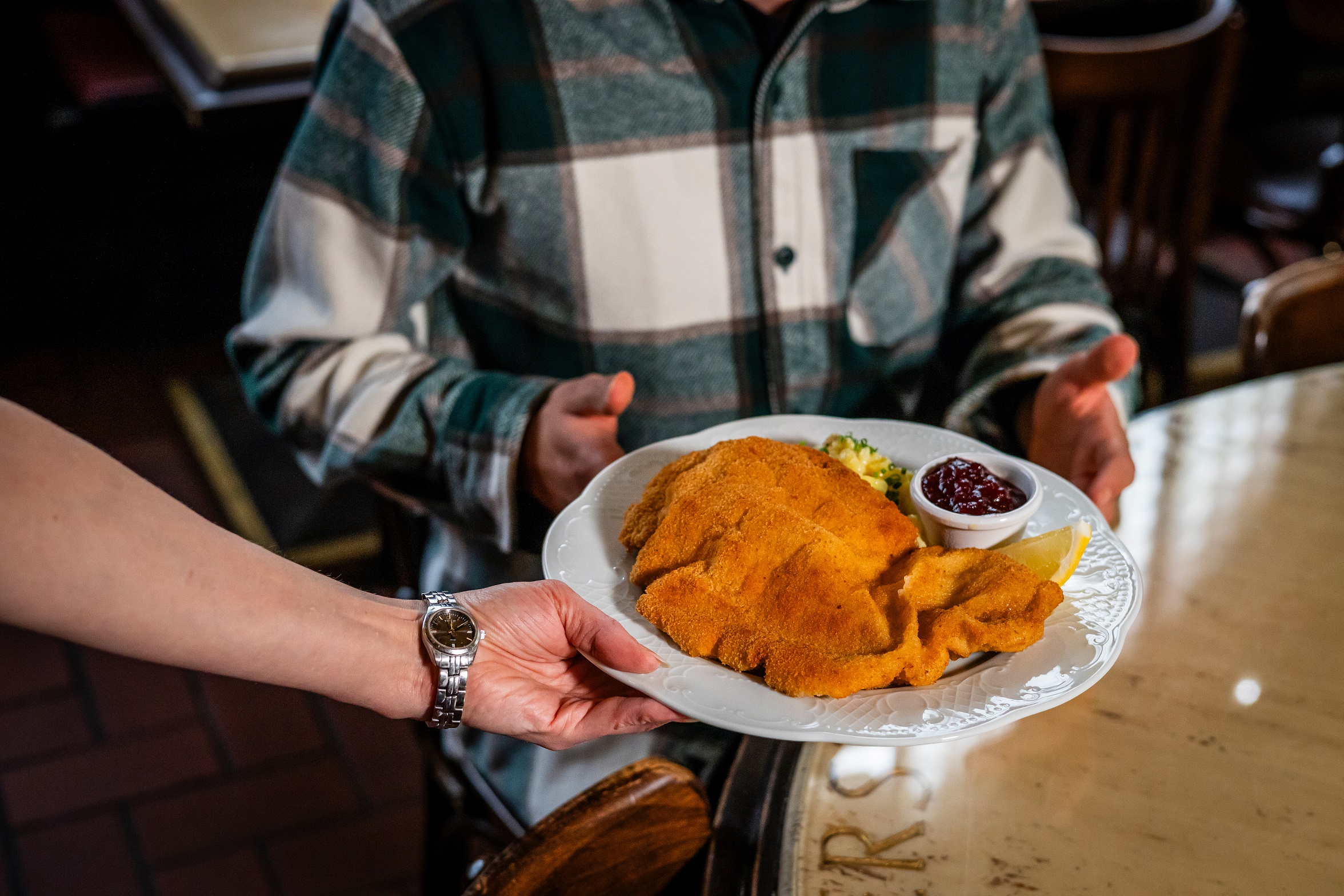  Kellnerin serviert Mann ein Schnitzel mit Beilagen im Restaurant 