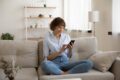 frau sitzt auf couch und schaut auf smartphone