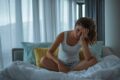 frau sitzt mit kopfschmerzen im bett
