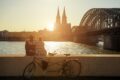 Ein Pärchen sitzt auf einer Mauer und schaut sich den Sonnenuntergang mit Blick auf den Kölner Dom an.